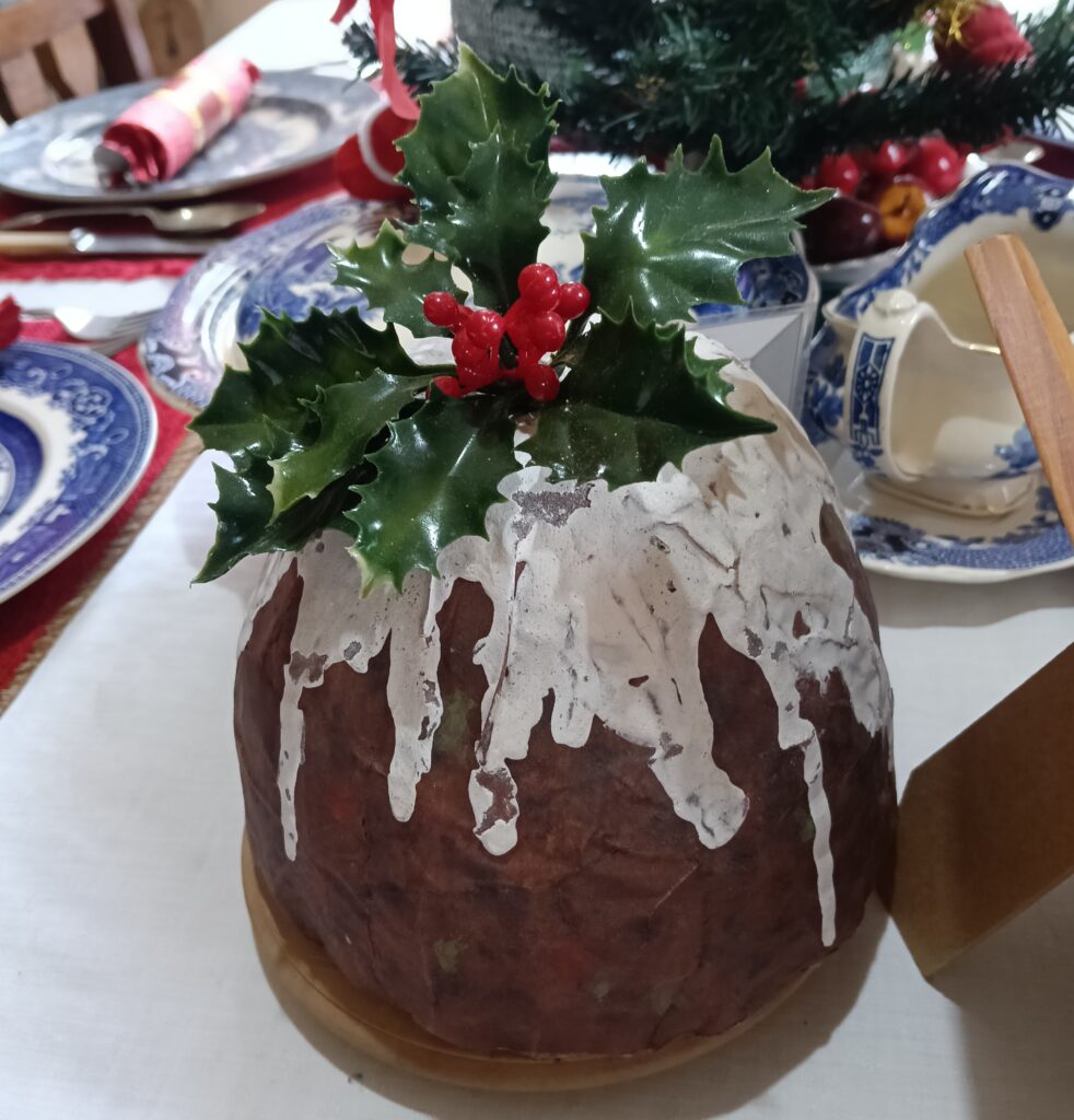 A Christmas pudding with cream dripping down the side and a sprig of holly with red berries on top.